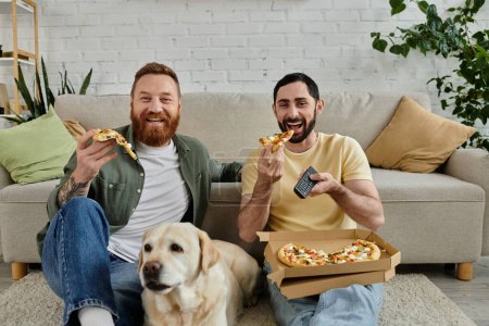 Two bearded men enjoy pizza on a couch with their labrador dog in the living room.