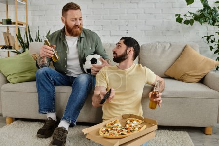 Foto de A men with a beard sits on a couch, holding a bottle of beer and a pizza - Imagen libre de derechos