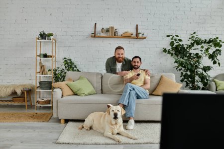 Two men, a bearded gay couple, sit on a couch petting their labrador in a cozy living room setting.