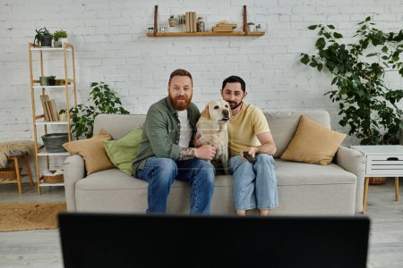 Photo for Two men, a bearded gay couple, sit contentedly on a couch with their Labrador retriever in a cozy living room. - Royalty Free Image