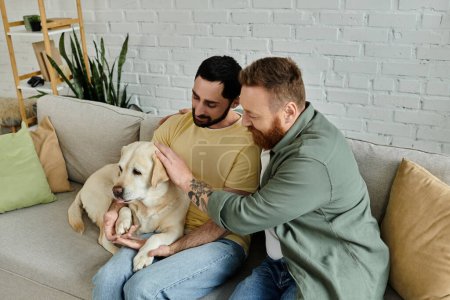 Two bearded men sit on a couch, lovingly petting a Labrador in a cozy living room setting.