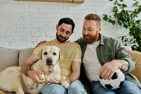 Foto de Bearded gay couple cuddle with their labrador on a cozy couch in their living room, sharing a moment of tranquility. - Imagen libre de derechos