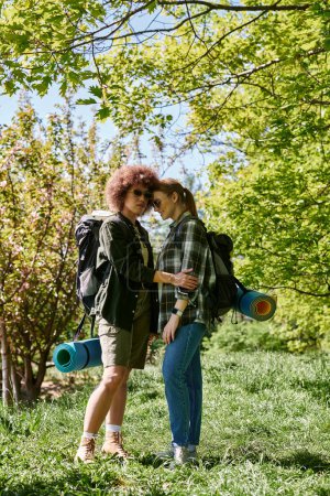 A young lesbian couple with backpacks hikes through the woods, enjoying a day outdoors.