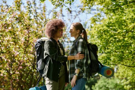 Zwei junge Frauen, ein lesbisches Paar, wandern gemeinsam in einem grünen Wald und genießen einen sonnigen Tag im Freien.