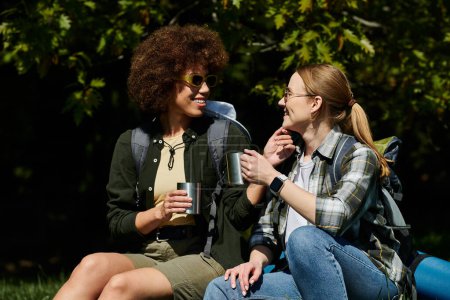 Two young women, a lesbian couple, enjoy a coffee break during a hike through the woods.