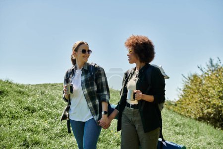 Two young women, a lesbian couple, are hiking together on a sunny day. They are smiling and holding hands, enjoying their time in the wilderness.