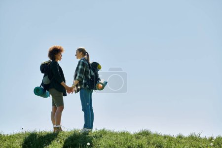 A young lesbian couple, holding hands, hikes on a sunny day.