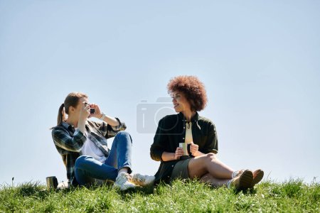 Two young women, a lesbian couple, are hiking and enjoying a break together on a grassy hill.