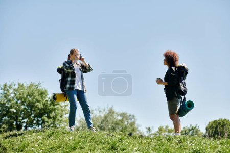 Photo for Two young women, a lesbian couple, are hiking in the wilderness, one taking a picture of the other. - Royalty Free Image