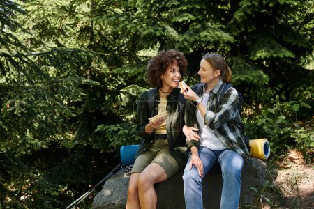 Photo for Two young women, a lesbian couple, are hiking together and enjoying a snack break in the wilderness. - Royalty Free Image