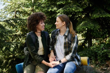 A young lesbian couple enjoys a hike through the woods, taking a break to rest and share a moment of intimacy.