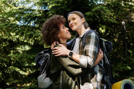 A young, multicultural lesbian couple embraces during a hike in the woods, showcasing their love and connection amidst natures beauty.