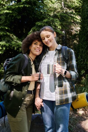 Ein lesbisches Paar genießt eine Wanderung im Wald, hält Händchen und trinkt aus seinen Thermoskannen.