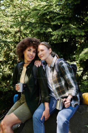 Two young women, one with curly brown hair and one with straight blonde hair, are hiking in the woods together.
