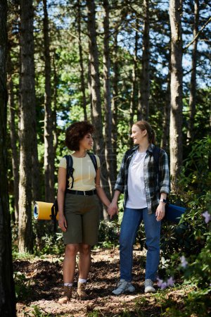 Una joven pareja lesbiana camina por un bosque, de la mano, disfrutando de un día soleado.