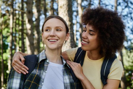 Zwei junge Frauen, ein lesbisches Paar, wandern durch einen Wald und teilen einen glücklichen Moment miteinander.