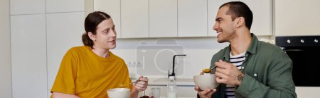 Ein junges schwules Paar sitzt an einem Küchentisch und genießt ein gemeinsames Essen in seiner modernen Wohnung.
