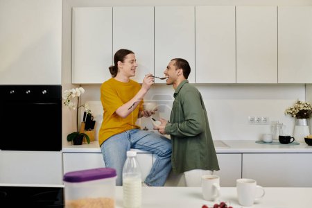 A young gay couple enjoys a playful moment in their modern kitchen, sharing breakfast and laughter.