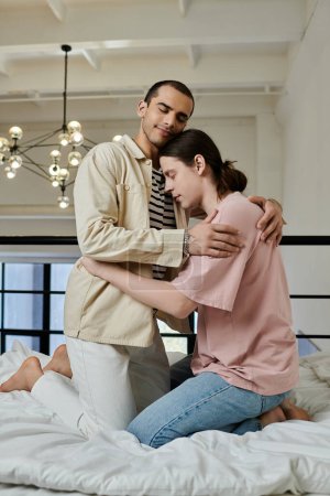 A young gay couple embraces on a white bed in their modern apartment.