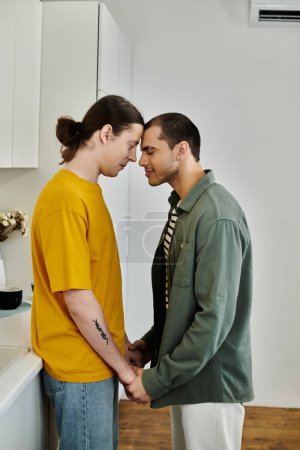 Photo for Two young men in casual attire stand close together in a modern apartment, their foreheads touching in a gesture of love and connection. - Royalty Free Image
