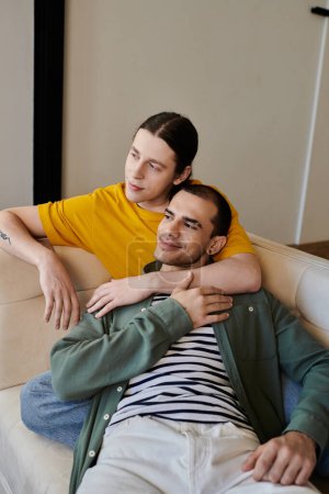A young gay couple relaxes on a couch in their modern apartment.