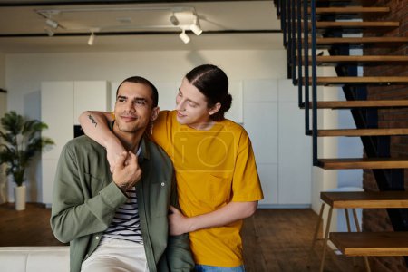 Ein junges schwules Paar in lässiger Kleidung genießt die Zeit in einer modernen Wohnung mit Holztreppe.