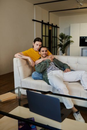Ein junges schwules Paar entspannt sich auf einem weißen Sofa in seiner modernen Wohnung und verbringt viel Zeit miteinander.