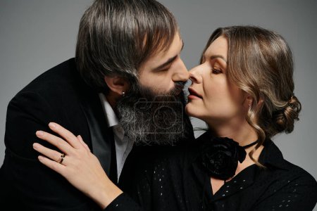 Un hombre y una mujer, vestidos con sofisticado atuendo negro, abrazan y comparten un momento tierno.