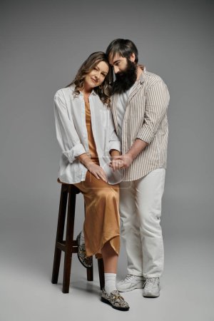 Un couple amoureux pose ensemble dans un cadre studio, mettant en valeur leur tenue sophistiquée et leur connexion intime.