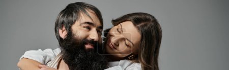 Un couple amoureux en tenue sophistiquée s'embrasse devant une toile de fond grise.