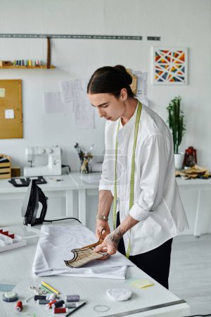 Ein junger Mann im weißen Hemd arbeitet in seinem Atelier an einem Kleiderrestaurierungsprojekt, das sich auf Nachhaltigkeit und die Wiederbelebung ausrangierter Kleidungsstücke konzentriert.