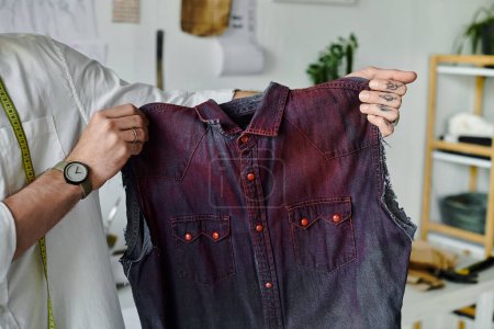 Un jeune homme tient une chemise en denim restaurée dans son atelier de restauration des vêtements, axée sur la durabilité et donnant une nouvelle vie aux vieux vêtements.