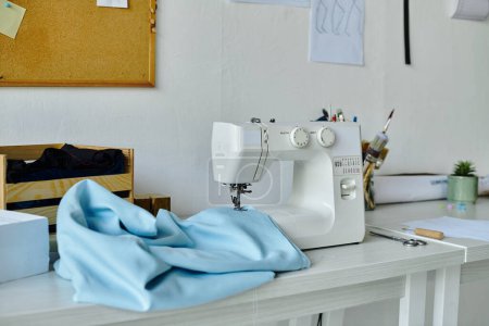 An einem sauberen, weißen Arbeitsplatz steht eine weiße Nähmaschine bereit. Ein Stück blauer Stoff liegt drapiert über dem Tisch, bereit, durch die Kunst der Kleiderrestaurierung zu neuem Leben erweckt zu werden.