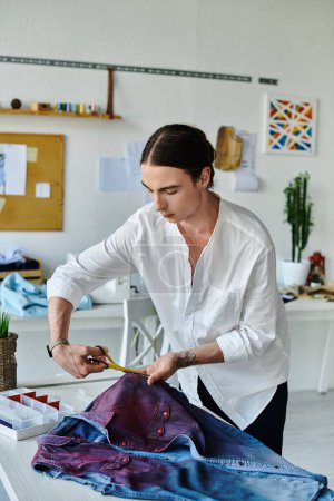 Ein junger schwuler Mann arbeitet in seinem Kleiderrestaurierungsatelier an einer Jeansjacke.