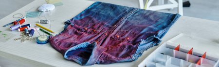 A close-up of a colorful, upcycled denim shirt, laying on a table with sewing supplies.