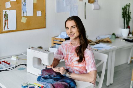 Un joven, vestido con una camisa de tinte, sonríe mientras trabaja en una máquina de coser en su taller de restauración de ropa.