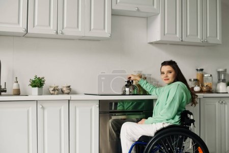 Une jeune brune en fauteuil roulant prépare le dîner dans sa cuisine. Elle porte un sweat vert et un pantalon blanc.