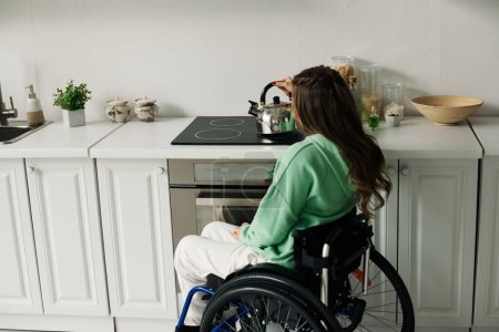 Une jeune femme en fauteuil roulant prépare le thé à la maison dans sa cuisine.