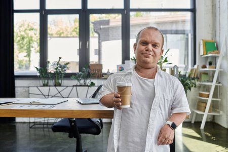 Un hombre con inclusividad se para en una oficina, sosteniendo una taza de café, con una sonrisa confiada.