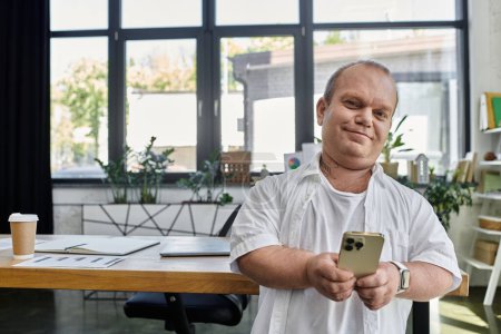 Ein inklusiver Mann im Büro lächelt in die Kamera, während er ein Smartphone in der Hand hält.