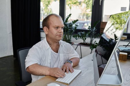 Ein Mann mit Inklusion sitzt an einem Schreibtisch und arbeitet in einem hellen, modernen Büroraum fleißig am Computer..