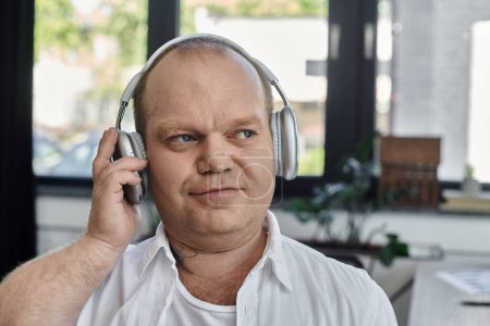 A man with inclusivity wearing headphones adjusts them while sitting in an office.