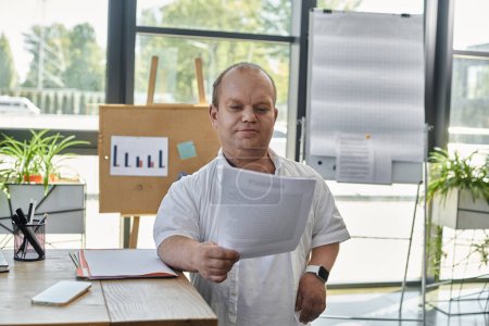 Un hombre con inclusividad en una camisa blanca está junto a un escritorio, revisando cuidadosamente los documentos en una oficina moderna.