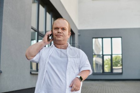 Un homme inclusif marche en toute confiance vers une fenêtre, parlant sur son téléphone.