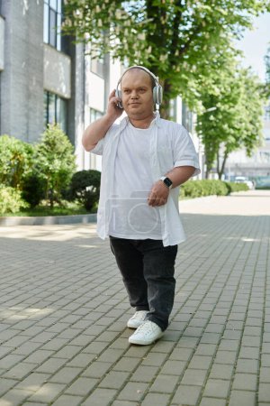 A man with inclusivity walks down a city street, listening to music through headphones.