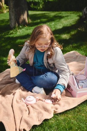 A little girl with Down syndrome enjoys a tea party with her doll in the park.