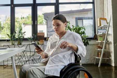A young businesswoman with a disability sits in a wheelchair, working in a modern office.