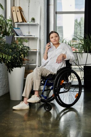 A young businesswoman, sitting in a wheelchair, works in a modern office setting.