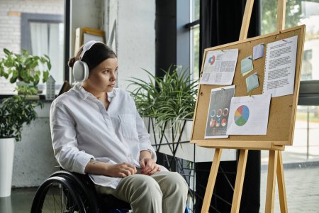 Une jeune femme d'affaires handicapée est assise dans un fauteuil roulant et travaille dans un bureau moderne.