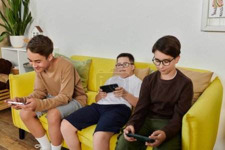 Téléchargez les photos : Trois jeunes garçons sont assis sur un canapé jaune, jouer à des jeux sur leurs téléphones. - en image libre de droit